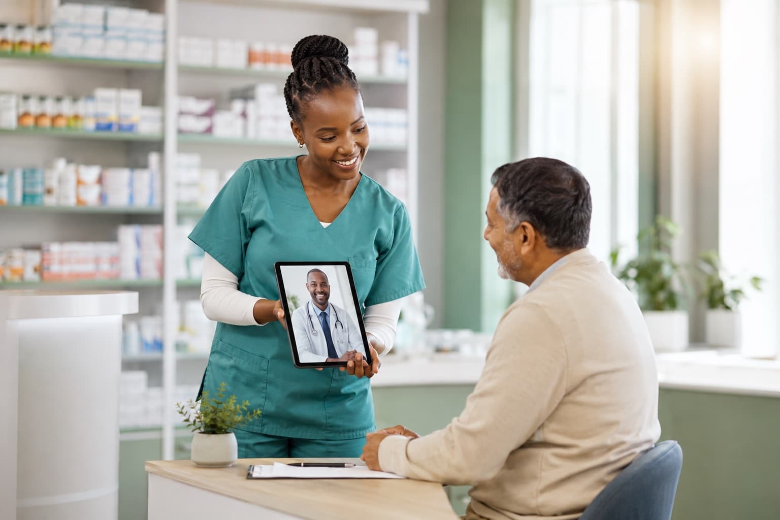 A nurse in a pharmacy clinic showing a patient a tablet with a doctor on a video call
