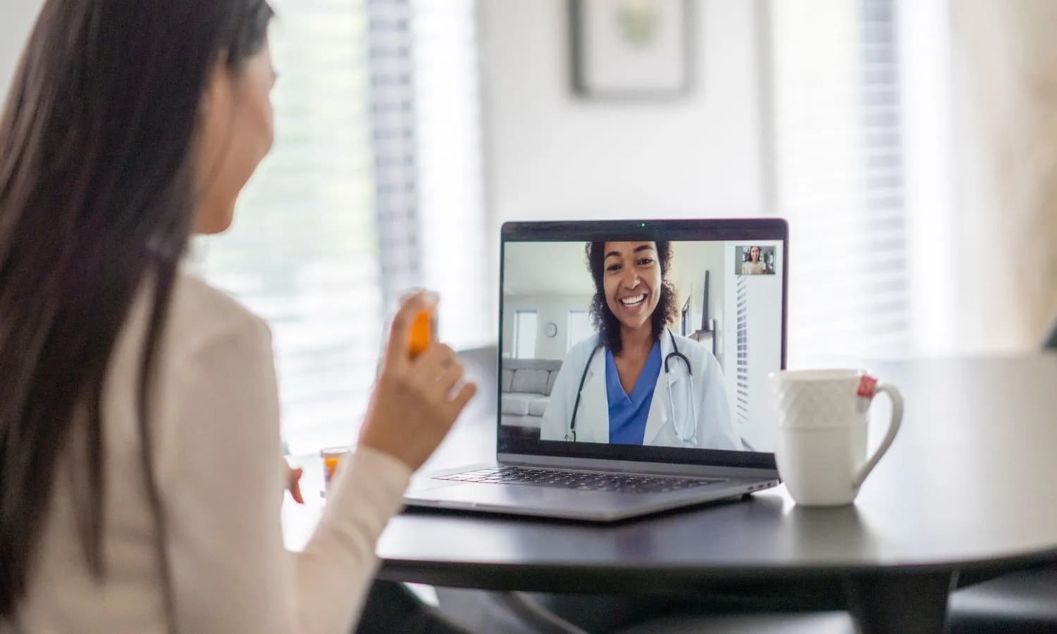 A patient holding a medication bottle during a video consultation with a doctor