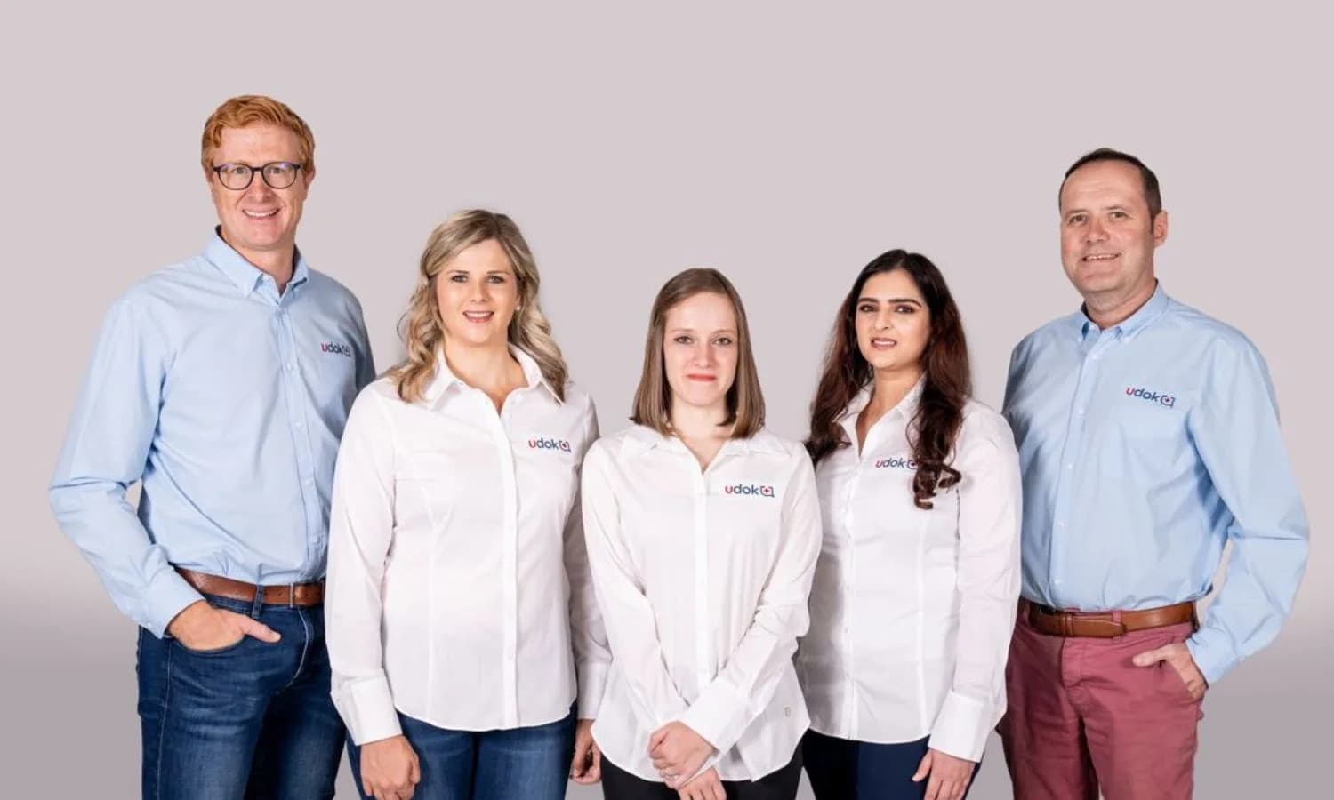Five Udok team members posing together in branded shirts