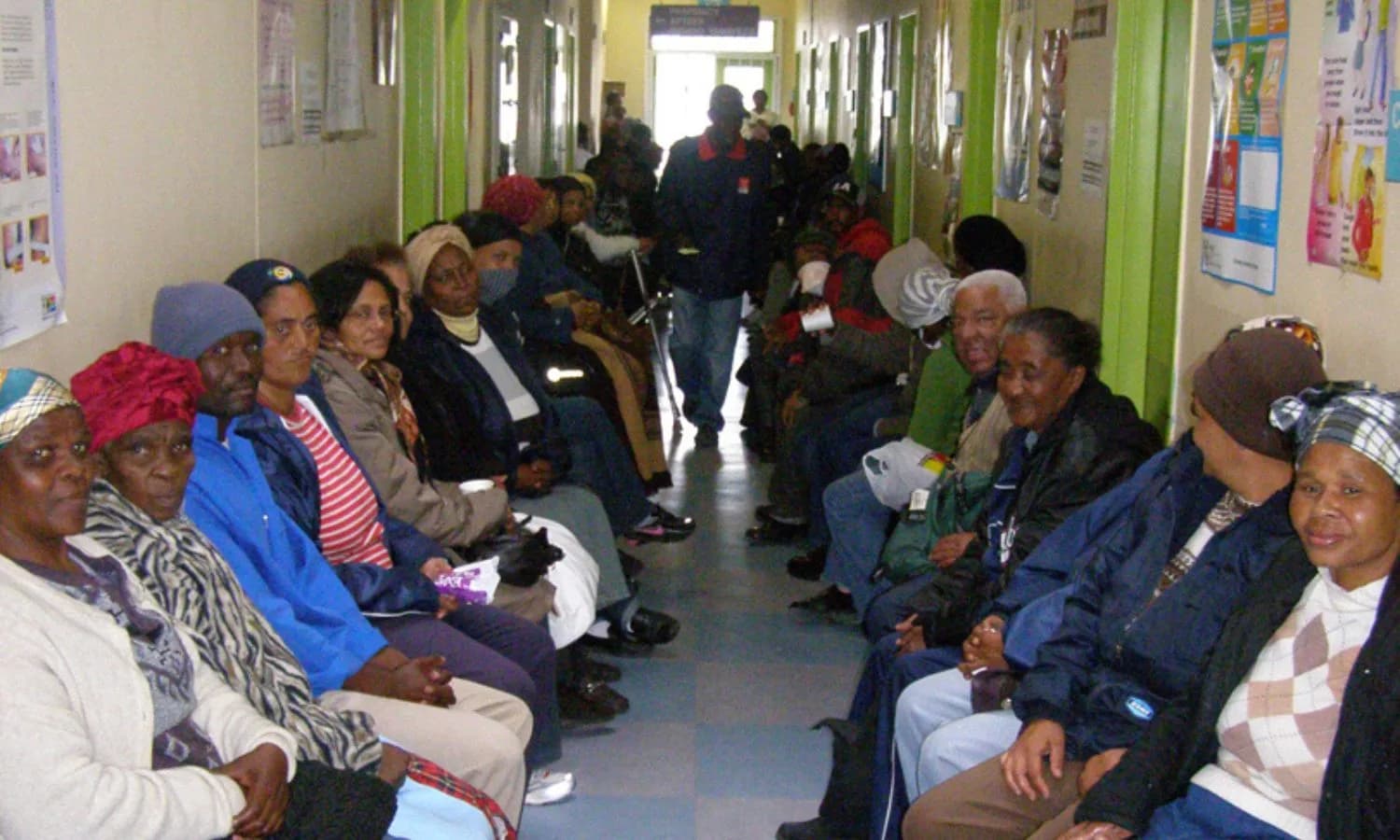 Patients seated along both sides of a crowded public clinic corridor