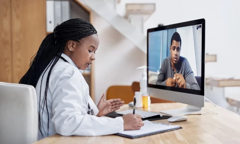A doctor taking notes while consulting a patient by video call